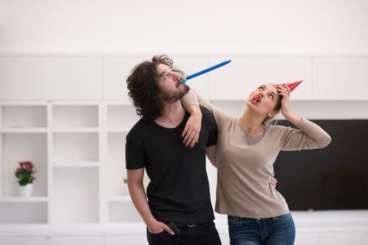 Young happy couple in party hats blowing in whistle isolated on a white background
