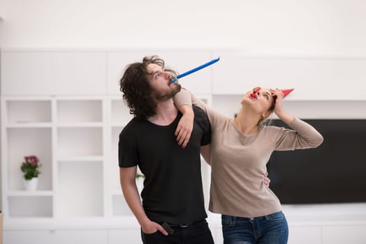 Young happy couple in party hats blowing in whistle isolated on a white background
