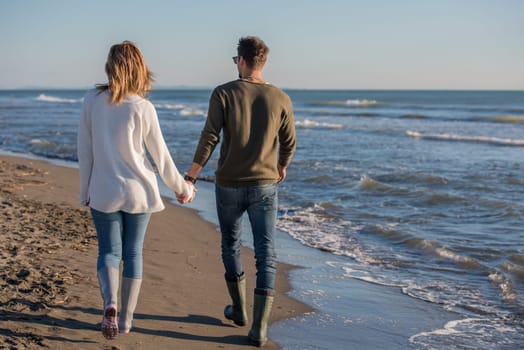 Young couple having fun walking and hugging on beach during autumn sunny day