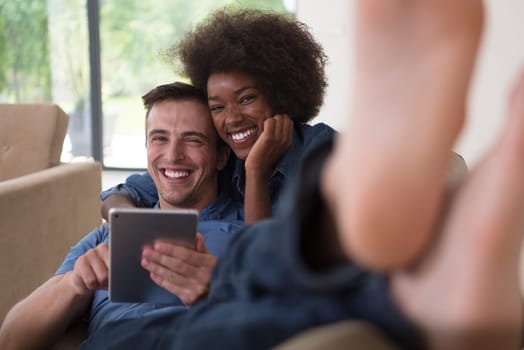 Young multiethnic couple relaxing at luxurious home with tablet computers reading in the living room on the sofa couch.