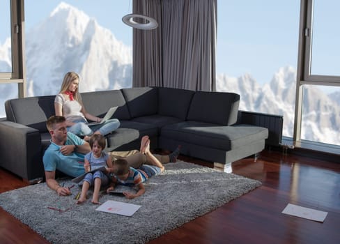 Happy Young Family Playing Together at home on the floor using a laptop computer and a children's drawing set