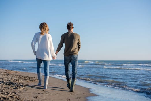Young couple having fun walking and hugging on beach during autumn sunny day