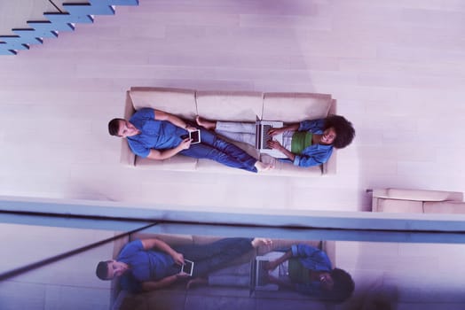 Young multiethnic couple relaxes in the luxury living room, using a tablet and laptop computer top view