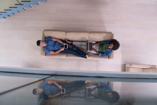 Young multiethnic couple relaxes in the luxury living room, using a tablet and laptop computer top view