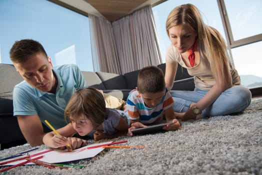Happy Young Family Playing Together at home on the floor using a tablet and a children's drawing set