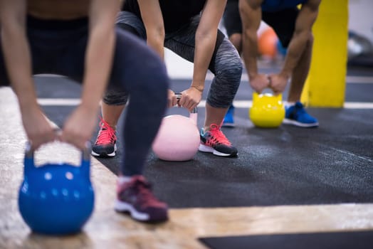 group of healthy young athletes doing exercises with kettlebells at cross fitness studio