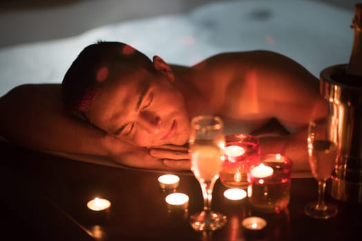 young handsome man enjoys relaxing in the jacuzzi with candles and champagne at luxury resort spa