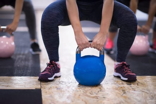 group of healthy young athletes doing exercises with kettlebells at cross fitness studio