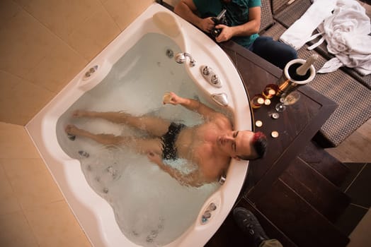 young handsome man enjoys relaxing in the jacuzzi with candles and champagne at luxury resort spa