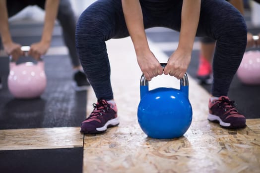 group of healthy young athletes doing exercises with kettlebells at cross fitness studio