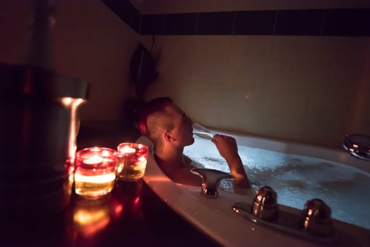young handsome man enjoys relaxing in the jacuzzi with candles and champagne at luxury resort spa
