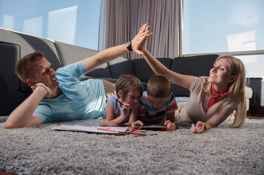 Happy Young Family Playing Together at home on the floor using a tablet and a children's drawing set