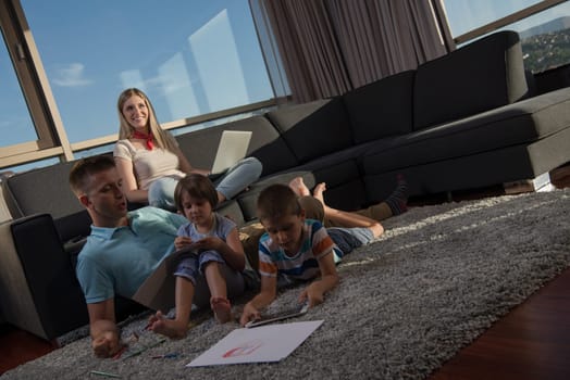 Happy Young Family Playing Together at home on the floor using a laptop computer and a children's drawing set
