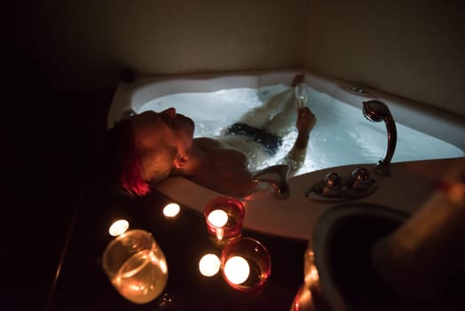 young handsome man enjoys relaxing in the jacuzzi with candles and champagne at luxury resort spa