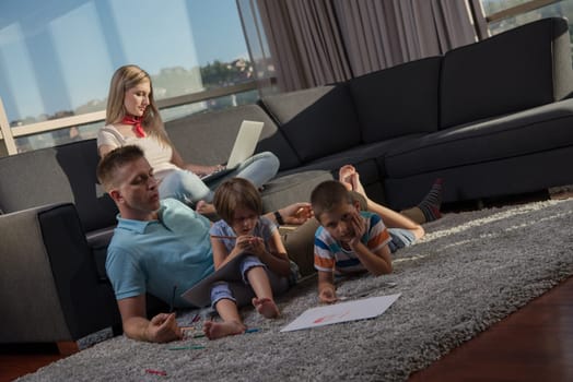 Happy Young Family Playing Together at home on the floor using a laptop computer and a children's drawing set
