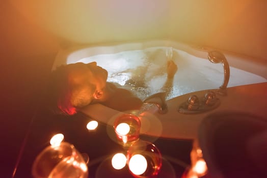 young handsome man enjoys relaxing in the jacuzzi with candles and champagne at luxury resort spa
