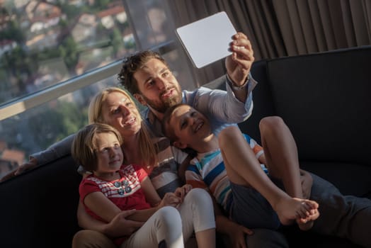 happy couple spending time with kids using tablet computer on sofa at home