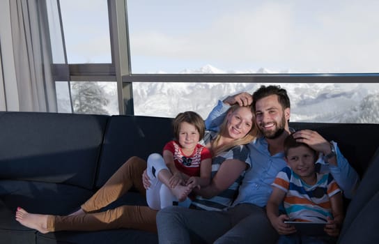 happy couple spending time with kids using tablet computer on sofa at home