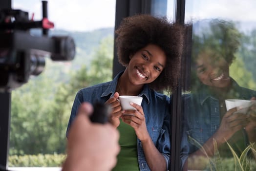 Beautiful young african american woman drinking coffee and looking through a window in her luxury home