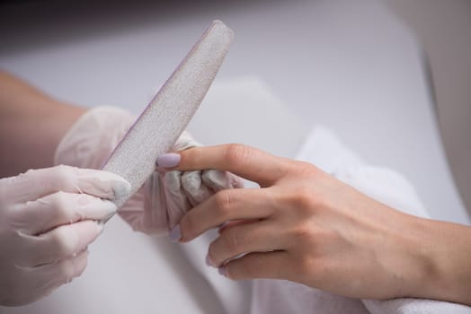 Woman hands receiving a manicure in beauty salon. Nail filing. Close up, selective focus.