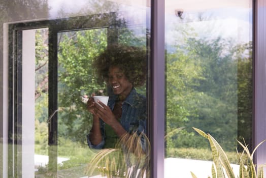 Beautiful young african american woman drinking coffee and looking through a window in her luxury home