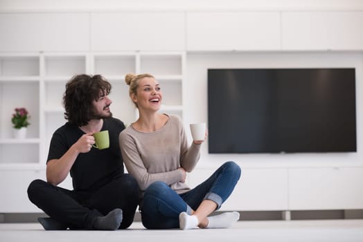 portrait of young happy beautiful couple sitting on the floor and drinking coffee in their new home