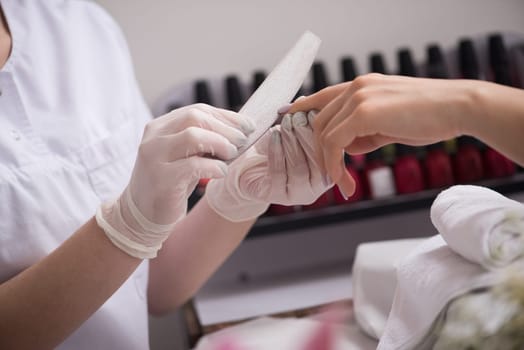 Woman hands receiving a manicure in beauty salon. Nail filing. Close up, selective focus.