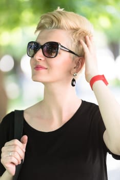 Beautiful fashionable young woman with short blond hair and sunglasses posing in the park