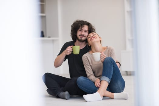 portrait of young happy beautiful couple sitting on the floor and drinking coffee in their new home