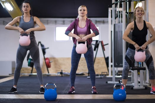 group of healthy young athletes doing exercises with kettlebells at cross fitness studio