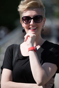 Beautiful fashionable young woman with short blond hair and sunglasses posing in the park