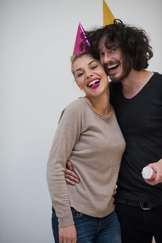 Young happy couple in party hats blowing in whistle isolated on a white background