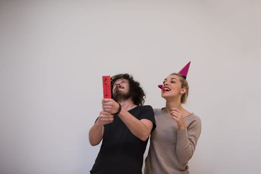 Young happy couple in party hats blowing in whistle isolated on a white background