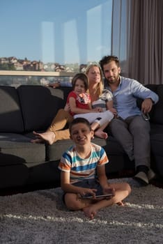 happy couple spending time with kids using tablet computer on sofa at home