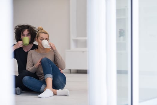 portrait of young happy beautiful couple sitting on the floor and drinking coffee in their new home