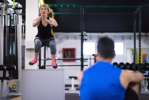 young athletic woman training with personal trainer  jumping on fit box at cross fitness gym