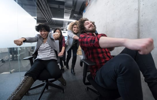 multiethnics startup business team of software developers having fun while racing on office chairs,excited diverse employees laughing enjoying funny activity at work break, creative friendly workers playing game together