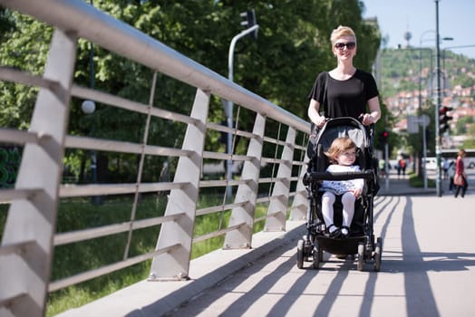 beautiful young mother with blond hair and sunglasses pushed her baby daughter in a stroller on a summer day