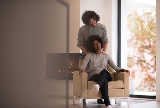 Young beautiful multiethnic couple hugging in front of fireplace at home when reading a book at autumn day