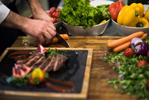 closeup of Chef hands in hotel or restaurant kitchen serving beef steak with vegetable decoration