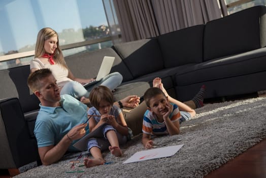 Happy Young Family Playing Together at home on the floor using a laptop computer and a children's drawing set