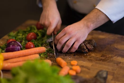 closeup of Chef hands in hotel or restaurant kitchen preparing beef steak with vegetable decoration