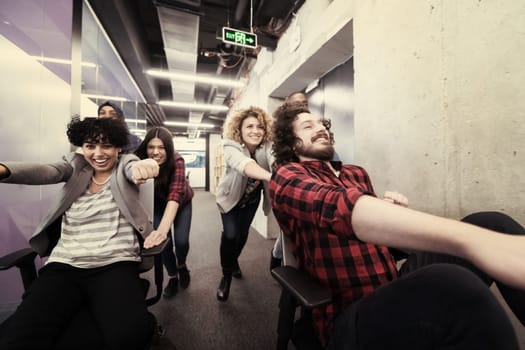 multiethnics startup business team of software developers having fun while racing on office chairs,excited diverse employees laughing enjoying funny activity at work break, creative friendly workers playing game together