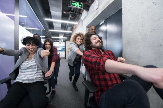multiethnics startup business team of software developers having fun while racing on office chairs,excited diverse employees laughing enjoying funny activity at work break, creative friendly workers playing game together
