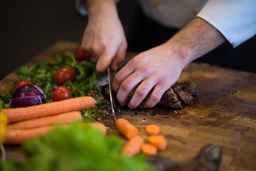 closeup of Chef hands in hotel or restaurant kitchen preparing beef steak with vegetable decoration