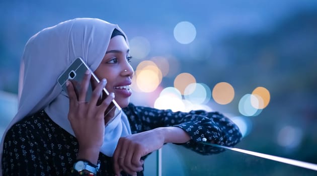 Young Muslim woman wearing scarf veil on urban city  street at night texting on smartphone with bokeh city light in background