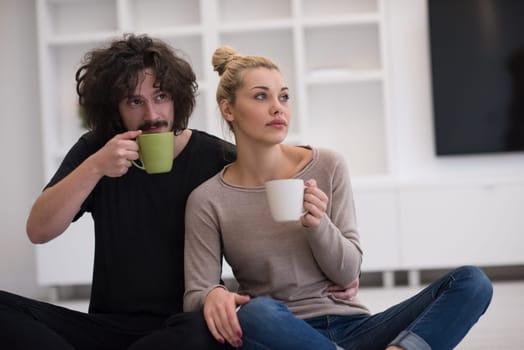 portrait of young happy beautiful couple sitting on the floor and drinking coffee in their new home