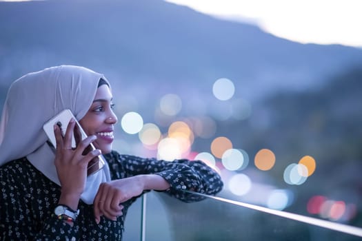Young modern Muslim woman wearing scarf veil on urban city  street at night texting on smartphone with bokeh city light in background