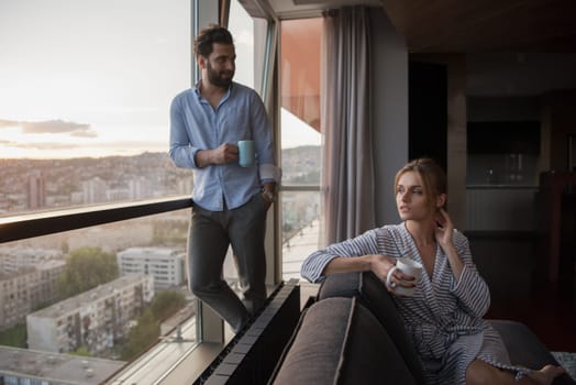 romantic happy young couple enjoying evening coffee and beautiful sunset landscape of the city while standing by the window