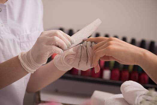 Woman hands receiving a manicure in beauty salon. Nail filing. Close up, selective focus.